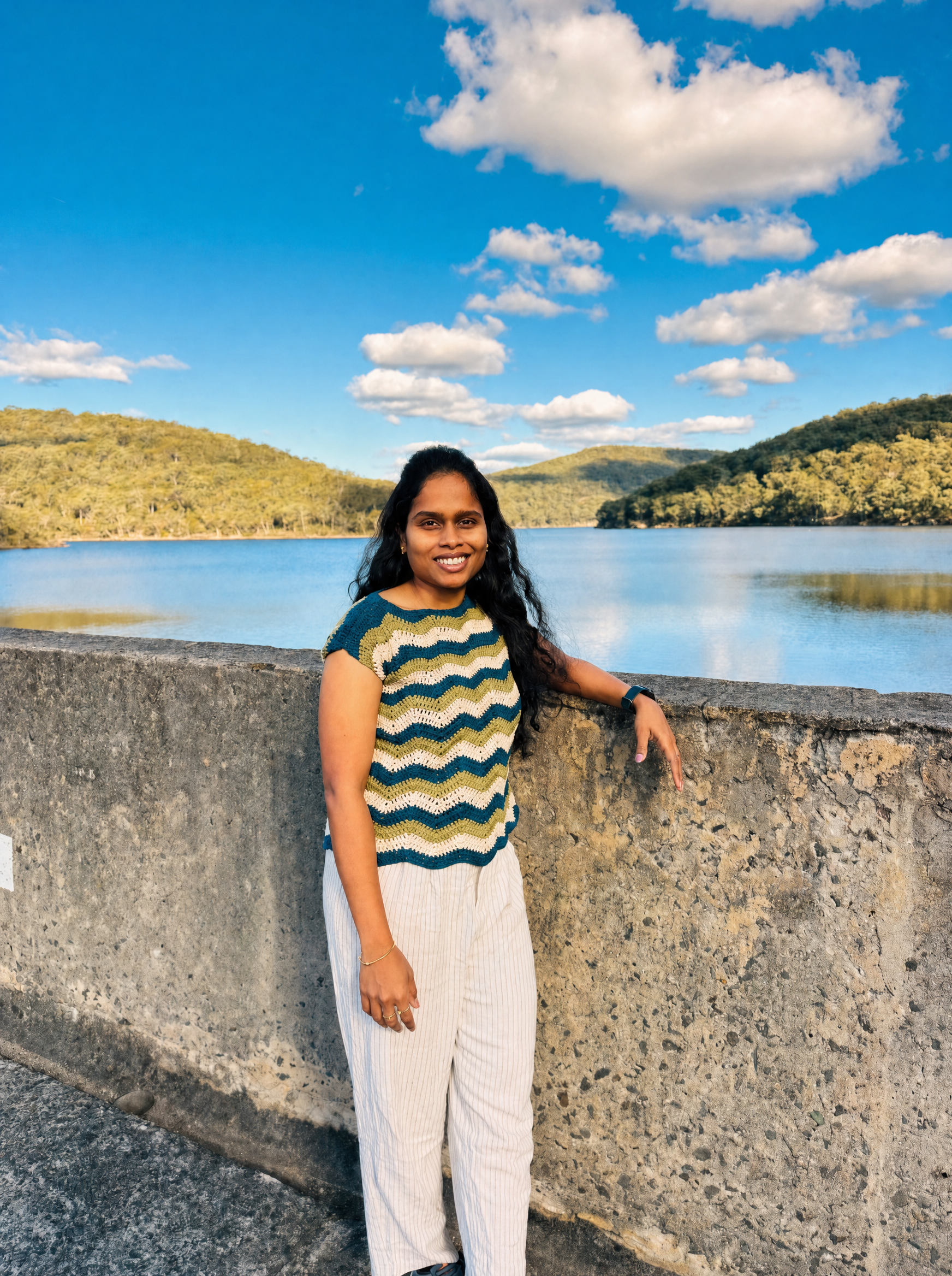 Chaitanya leaning on a wall overlooking a lake, wearing a colorful crochet top
